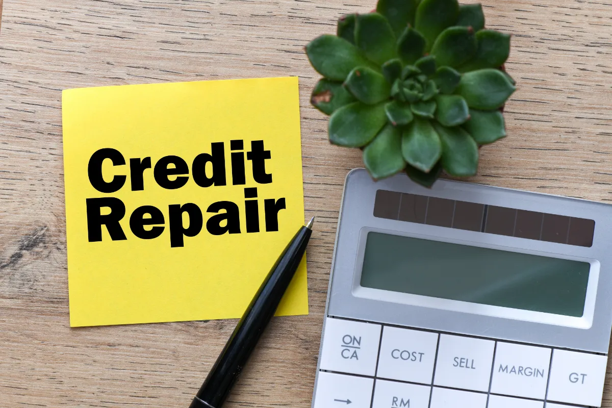 A "Credit Repair" sticky note, calculator, pen, and succulent on a desk