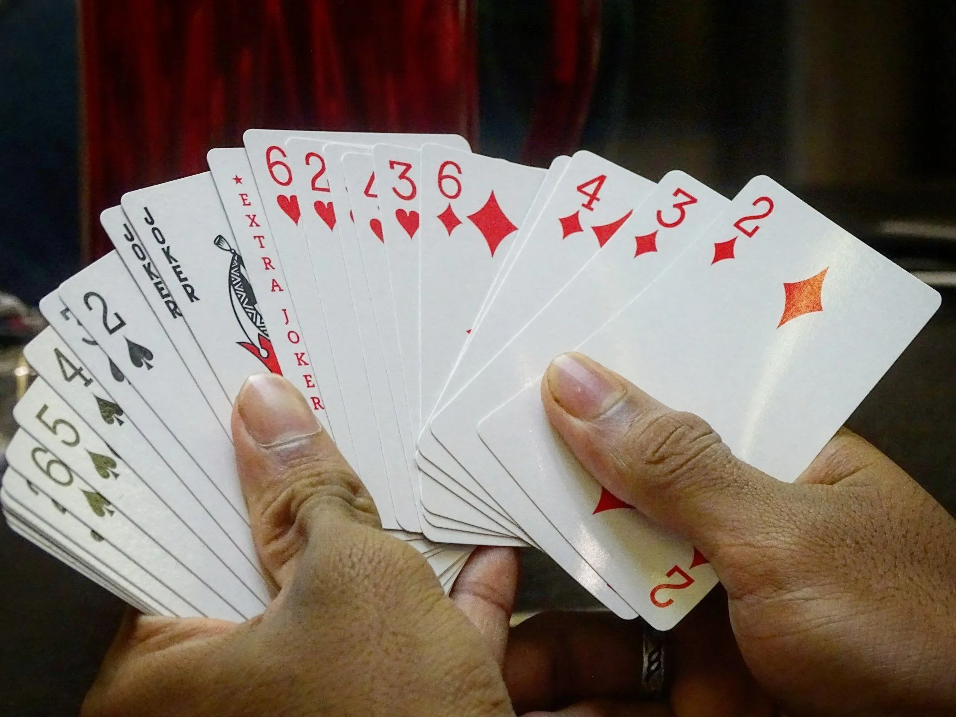 A hand holding playing cards fanned out, showing a joker and number cards.
