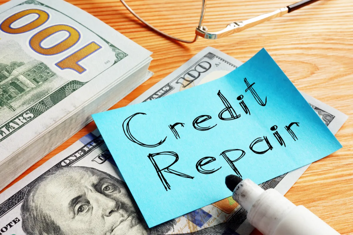 A note labeled "Credit Repair" with a marker, glasses, and cash on a table.
