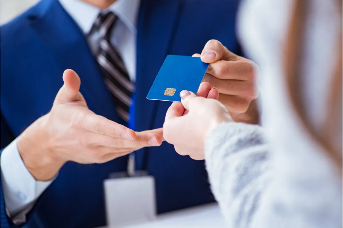 A person in a blue suit handing a blue credit card to someone.