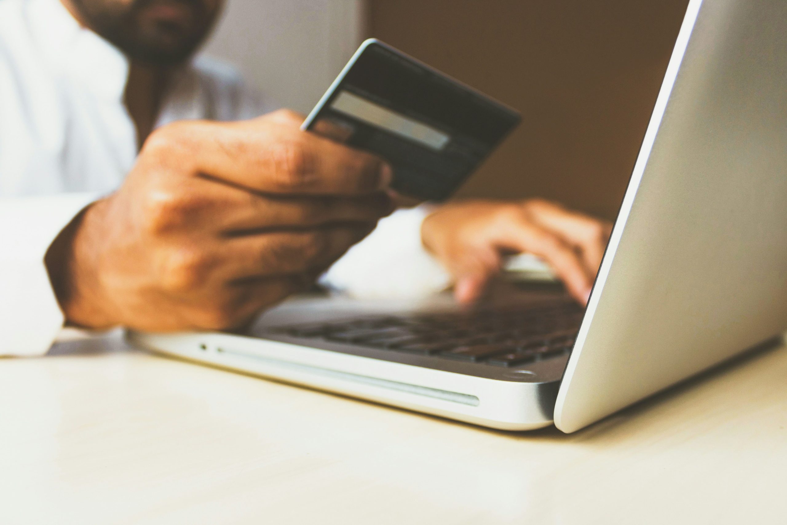 A person is holding a credit card and using a laptop, likely making an online purchase.