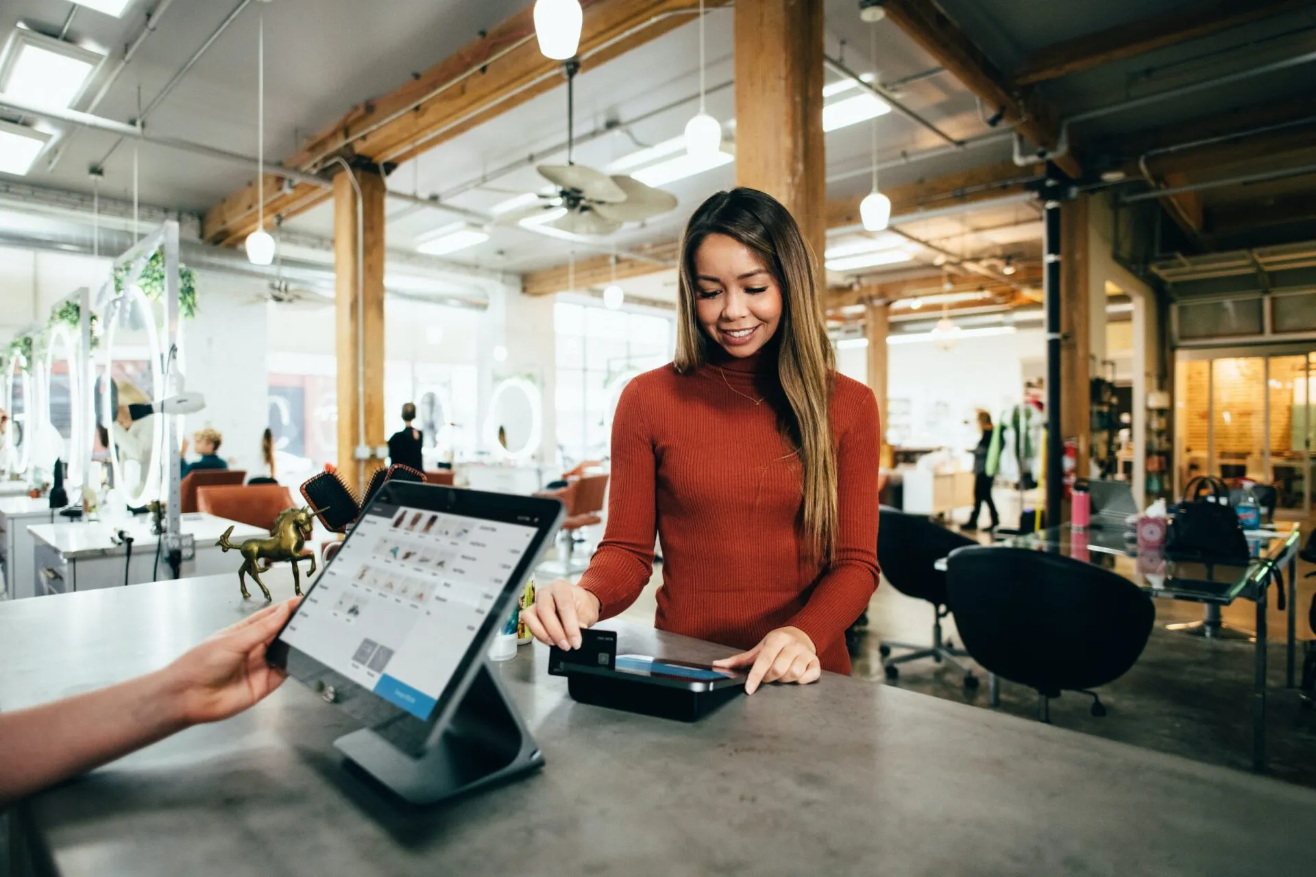 A woman in red uses a payment terminal in a bright, busy room.
