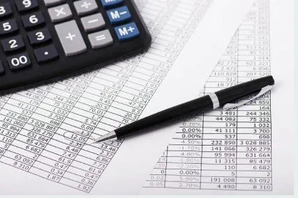 Calculator and pen on financial documents, indicating accounting or budgeting activity.