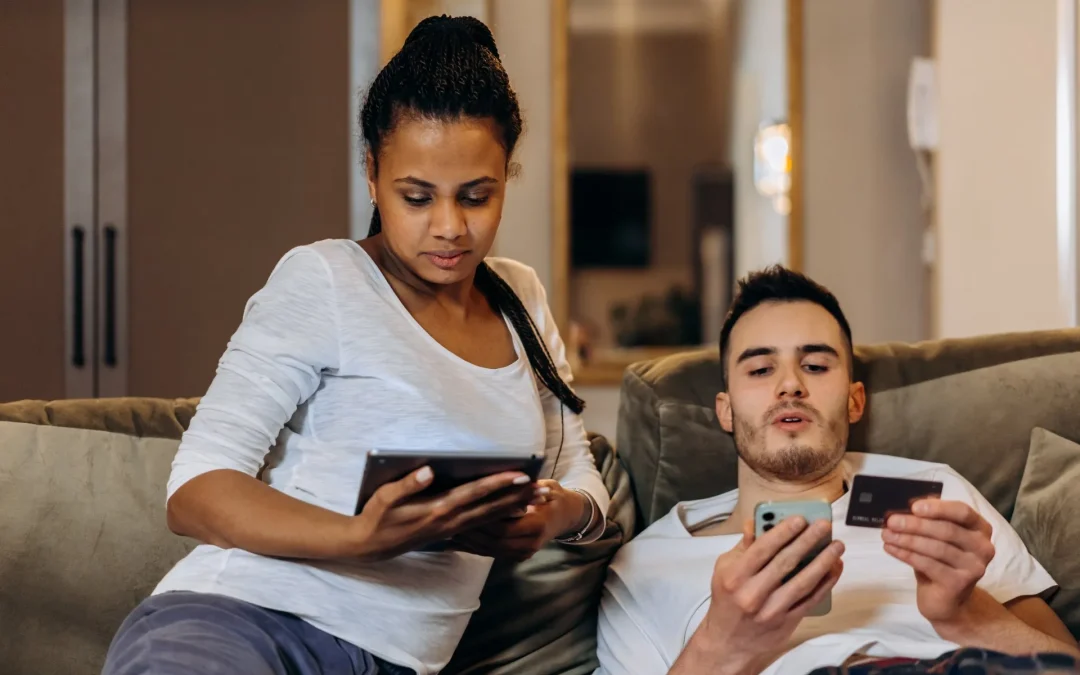 Couple on a couch using a tablet and a smartphone with a credit card.
