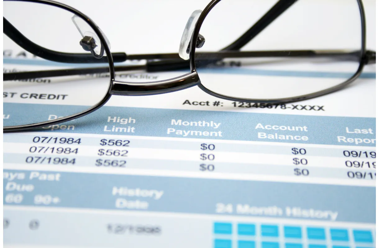 Eyeglasses on a credit report highlighting financial details and obscured account numbers.
