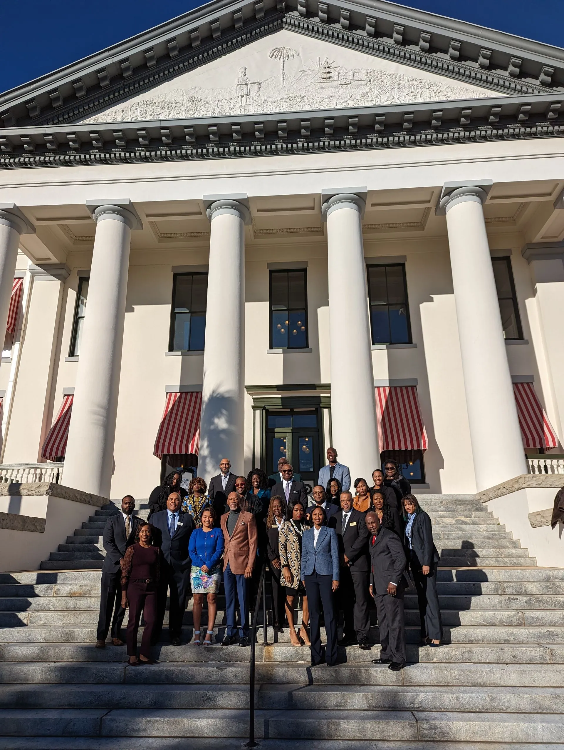 Group of people posing on the steps of a stately building with tall columns and a classical facade.