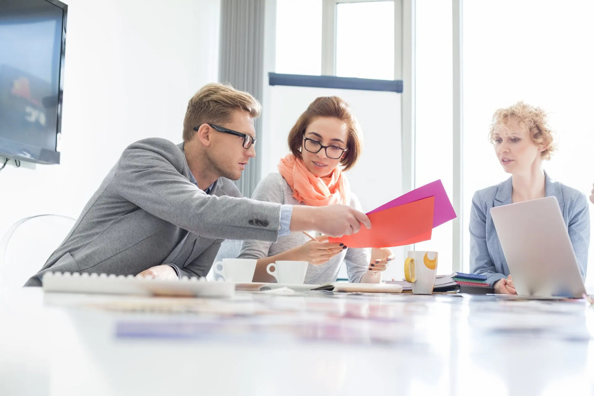 Three professionals examine documents at a bright office meeting table.